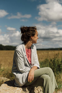 Full length of young woman sitting on rock looking into the distance