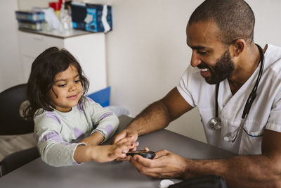 Smiling male pediatrician checking sugar level of girl in medical clinic