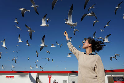 Low angle view of woman feeding seagulls flying against sky