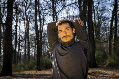 Runner is stretching while listening to music. young man is training in the woods.