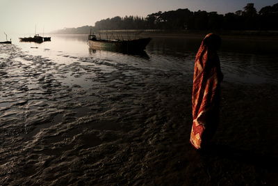 Full length of woman in sari standing by boat at riverbank