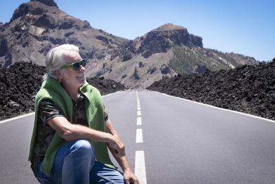 Smiling senior man sitting on road against mountain