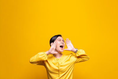 Woman shouting while standing against yellow background