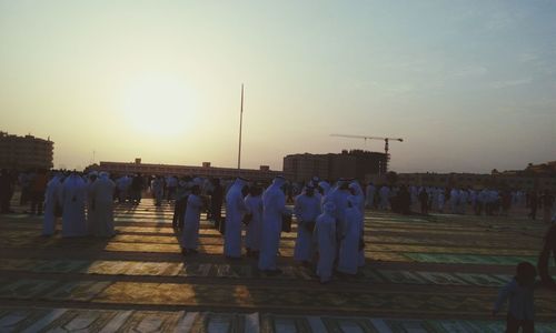 People in row against clear sky during sunset