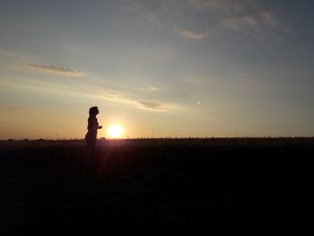 Side view of silhouette woman standing on field against sky during sunset