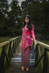 Young woman standing on footbridge against trees