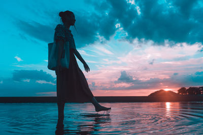 Woman standing by sea against sky during sunset