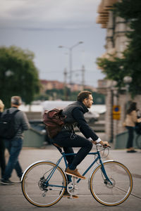 Side view of confident businessman riding bicycle on street in city
