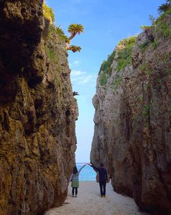 Rear view of man and woman standing amidst rock formation on beach at okinawa