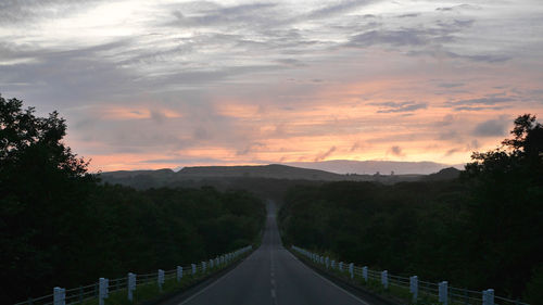 Road by trees against sky during sunset