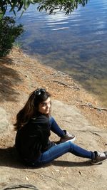 Side view of young woman sitting on shore