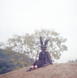 Woman wearing mask standing on field against sky