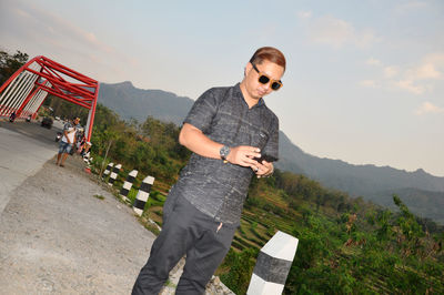 Full length of young man wearing sunglasses standing on mountain against sky