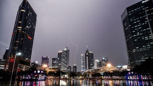 Illuminated cityscape by river against sky at night