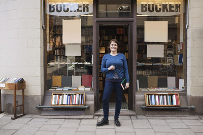 Full length portrait of smiling young woman standing at store