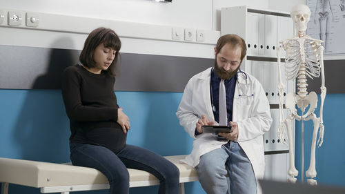 Doctor using digital tablet sitting by patient in hospital