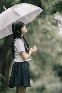 Young student with umbrella standing in park