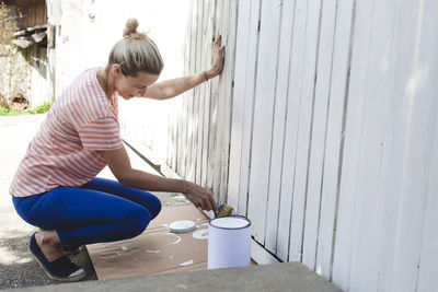 Smiling woman painting fence at yard