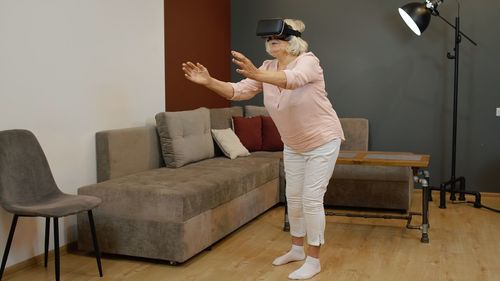 Senior woman using virtual reality simulator while standing at home
