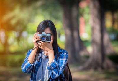 Young woman photographing from camera against trees