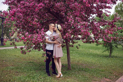 Portrait man and a woman in love stand by a blooming pink cherry tree in summer