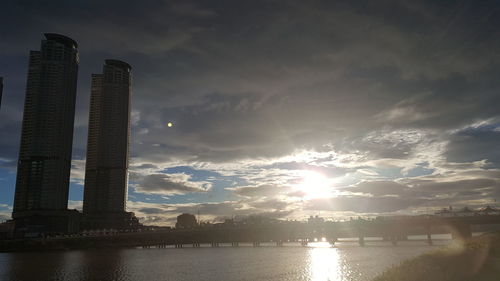 Scenic view of river by buildings against sky at sunset