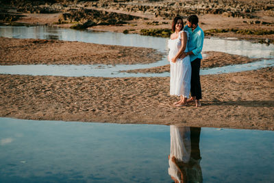 Full length of couple embracing while standing on beach against sky