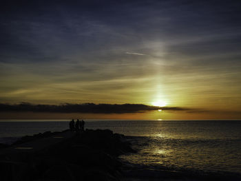 Silhouette people on beach against sky during sunset