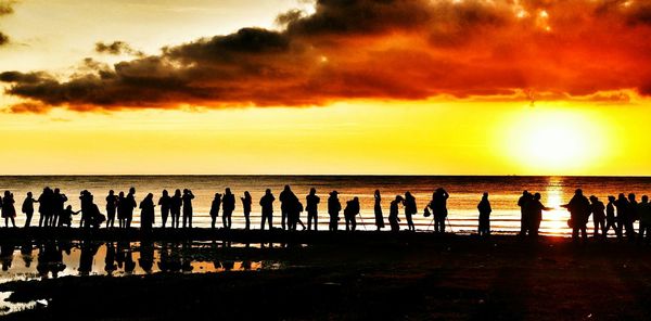 Silhouette of people standing on beach at sunset