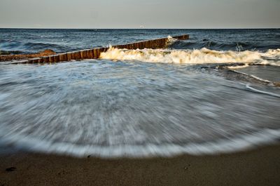 Waves rushing towards shore against sky