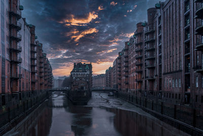 Buildings by river against sky during sunset