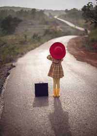 Rear view of girl with suitcase standing on road