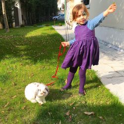 Smiling girl playing with rabbit on grassy field in yard