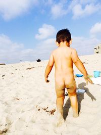 Rear view of naked boy walking on sand at beach against sky