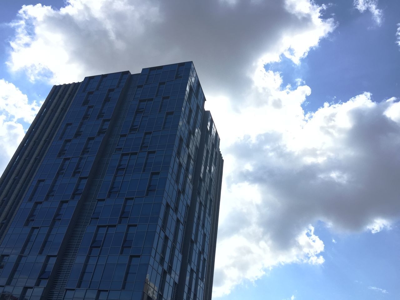 low angle view, sky, building exterior, architecture, built structure, cloud - sky, cloud, cloudy, building, day, outdoors, no people, city, blue, sunlight, tall - high, window, modern, pattern, high section