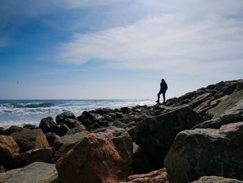 Man standing on rocks by sea against sky