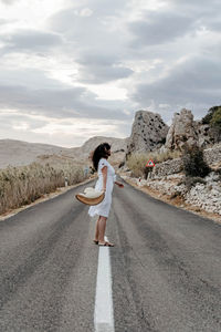 Rear view of young woman in white dress standing on road. summer, wanderlust, travel.