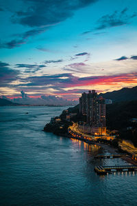 Illuminated buildings by sea against sky at sunset