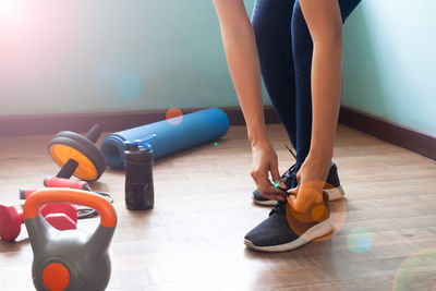 Low section of woman tying shoelace on hardwood floor at home