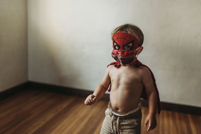 Full length of shirtless boy standing against wall at home