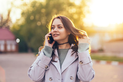 Beautiful girl with long hair in a grey trench coat using smartphone in the spring 