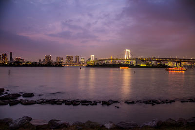 Illuminated city by river against sky at night