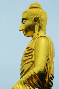 Low angle view of golden buddha statue against sky
