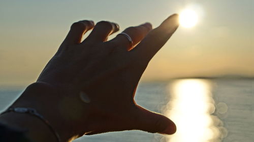 Close-up of man hand against sea during sunset