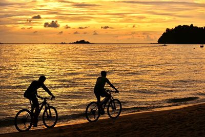 Silhouette people on beach against sky during sunset