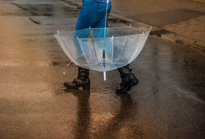 Low section of woman with umbrella walking on wet street during rainy season