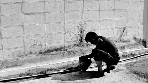 Side view of woman sitting on footpath against wall