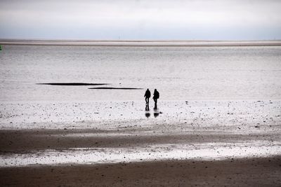 Mid distance view of silhouette men walking at beach against sky