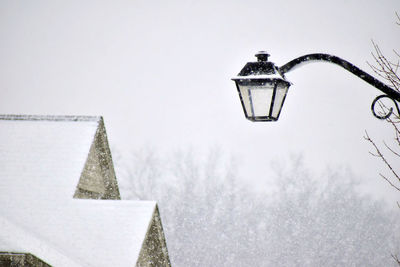 Low angle view of snow covered roof and street light against sky  amid storm 