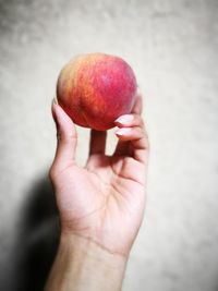 Close-up of woman hand holding apple against wall